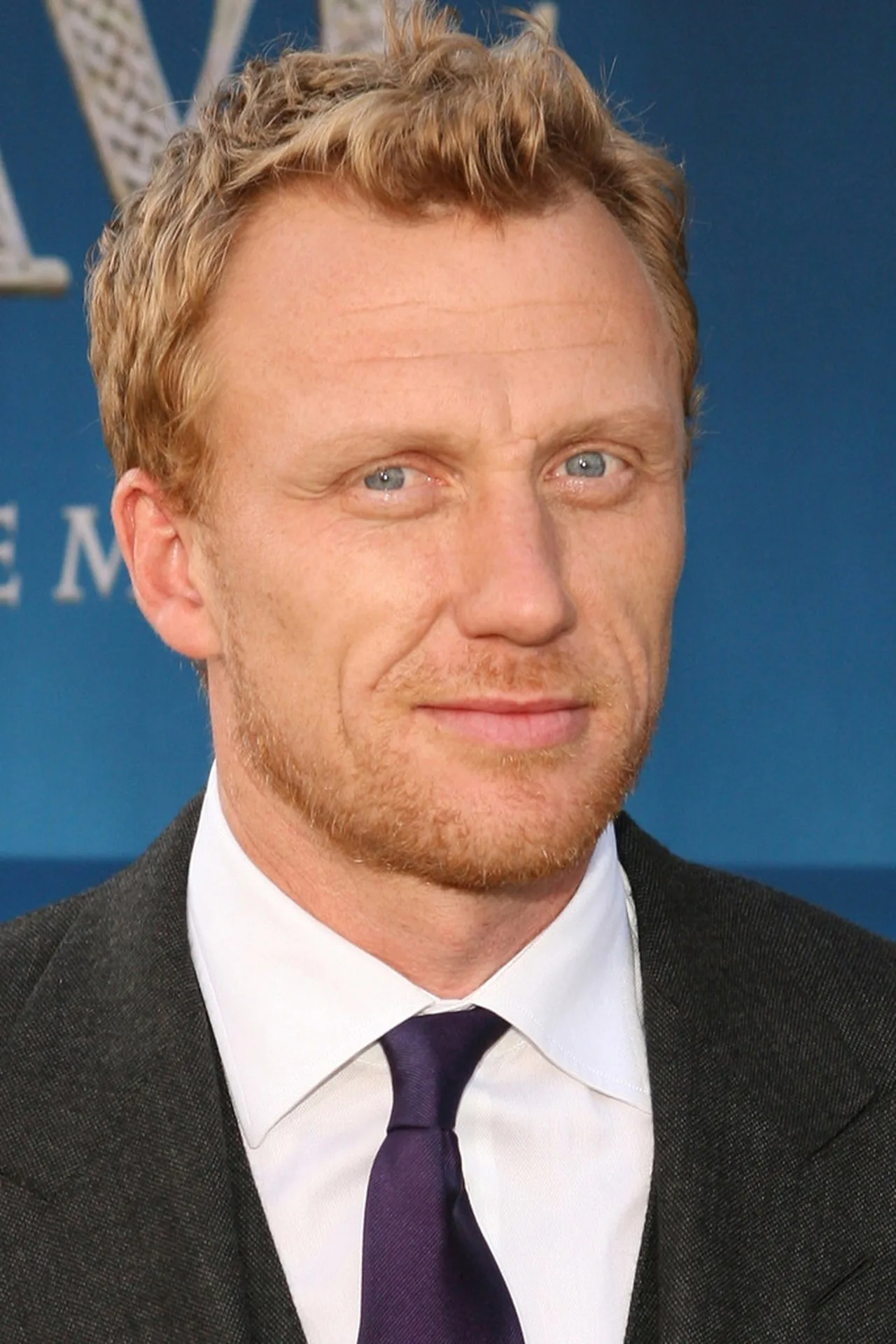 Kevin McKidd levanta halteres em uma academia, com uma garrafa de água e uma maçã verde sobre o banco de peso