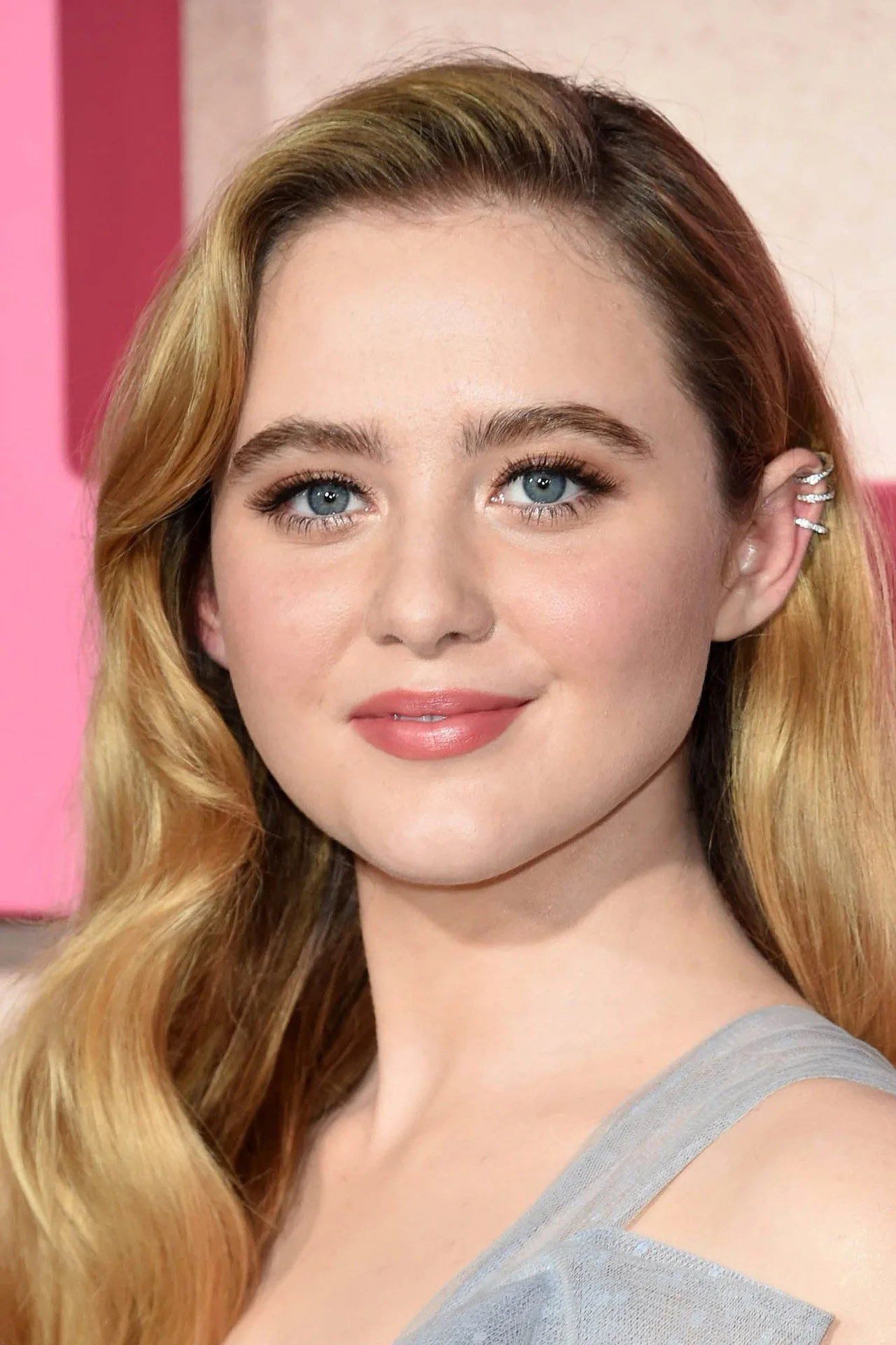 Kathryn Newton vestindo roupa de treino, segurando halteres enquanto faz agachamento, com pôster de Avengers ao fundo