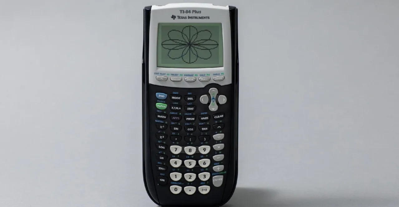 TI-84 Plus da Texas Instruments sobre uma mesa de aula, com seu logotipo e tela exibindo gráficos matemáticos