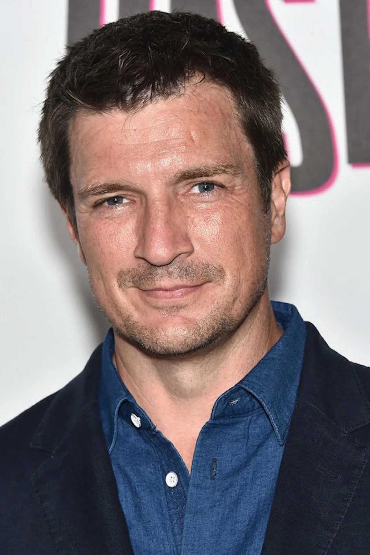 Nathan Fillion levantando halteres, exibindo seu novo corte de cabelo sob luz de academia