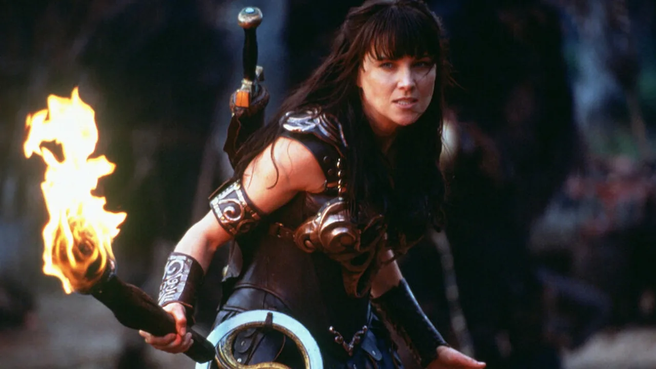 Lucy Lawless segurando uma espada de ferro enquanto faz agachamento com kettlebell ao lado