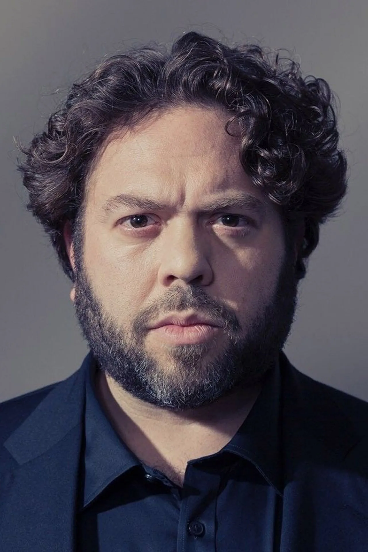 Ator Dan Fogler em traje de nobre, segurando espada, ao lado de kettlebells e garrafa d'água
