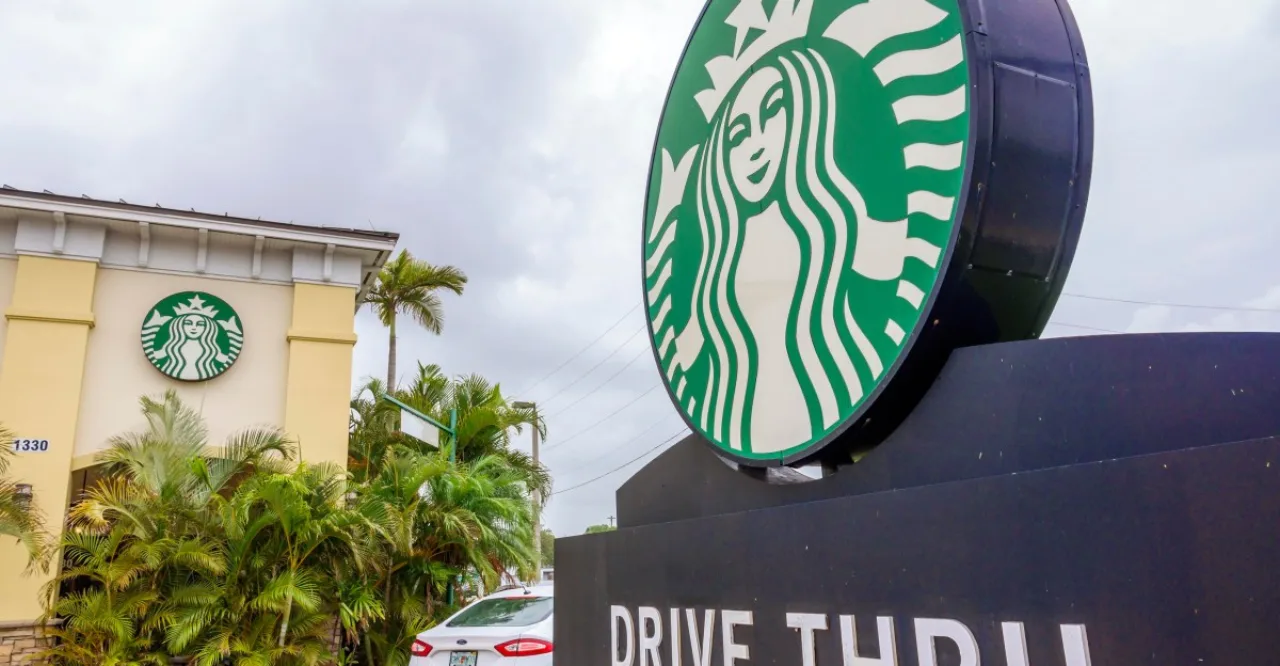 Tela digital no drive-thru exibe menu personalizado com logotipo da Starbucks e sugestões de bebidas para motorista no carro
