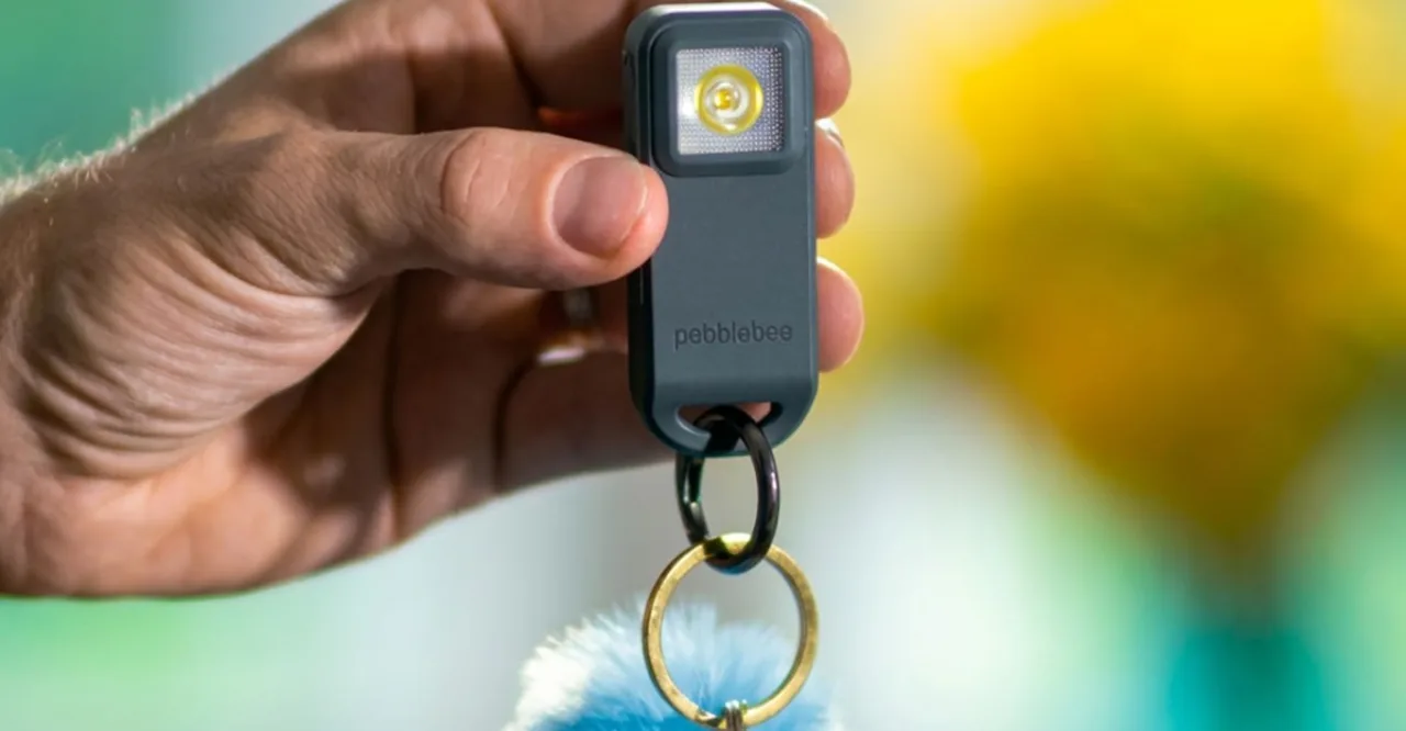 Pessoa caminhando ao ar livre segurando um chaveiro rastreador Pebblebee preso a uma mochila ou conjunto de chaves