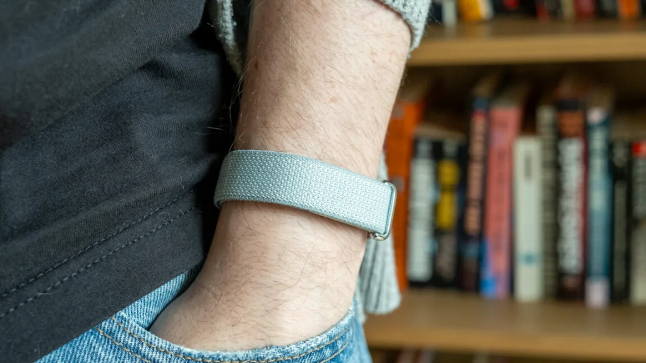 Braço masculino usando Fitbit Air discreto, sem tela, ao lado de um ícone de onda sonora representando IA da Google