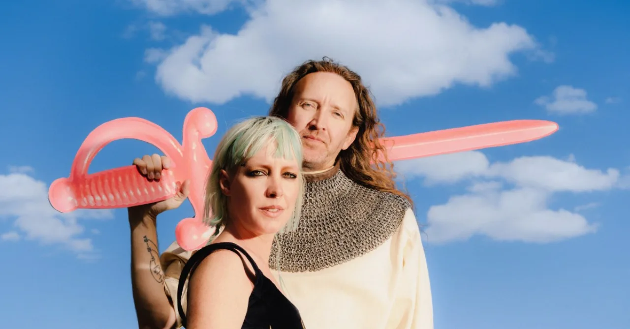 Amelia Meath e Nick Sanborn da Sylvan Esso seguram potes de iogurte, sorrindo em estúdio iluminado