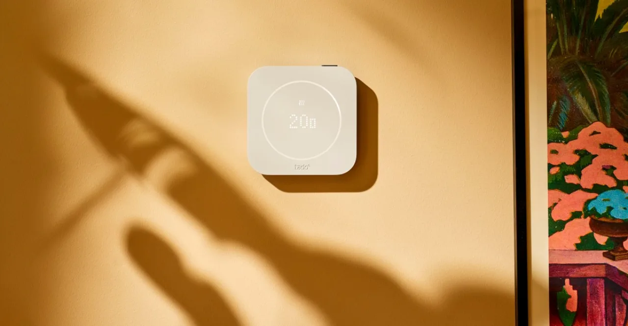 Jovem fazendo alongamento no tapete, vestindo roupa esportiva, ao lado do Tado Smart Thermostat X na parede
