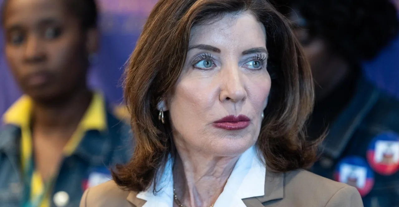 Kathy Hochul analisando um tablet com gráficos de IA ao lado de um haltere e uma maçã