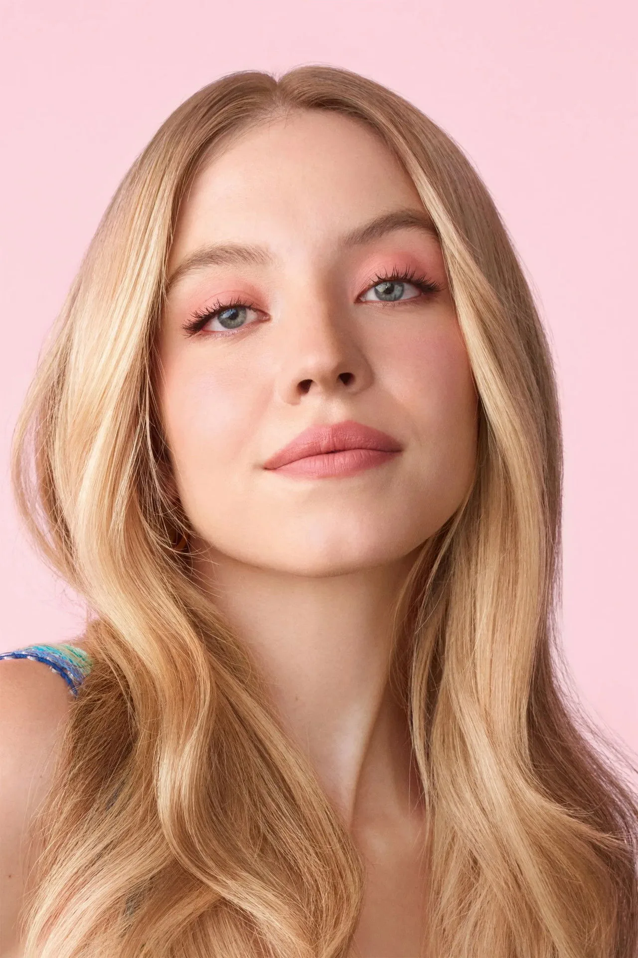 Sydney Sweeney vestindo roupa de academia, segurando um copo de água ao lado de halteres e tapete de yoga