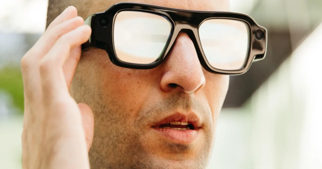 Um par de óculos Snap Specs sobre uma mesa, ao lado de um smartphone exibindo interface de realidade aumentada