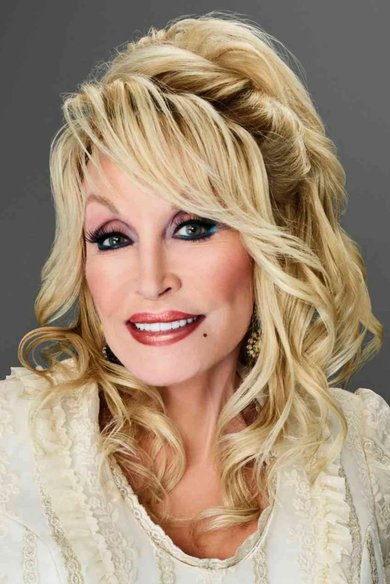 Mulher em traje de escritório alongando ao lado da mesa com laptop, copo d'água e foto de Dolly Parton ao fundo