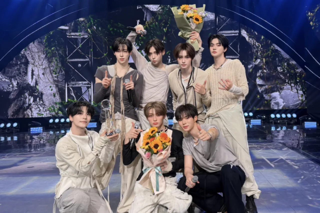 Jovem vestindo camiseta de Alpha Drive One levanta halteres ao som de “Born Dire”, com troféu Music Bank ao fundo
