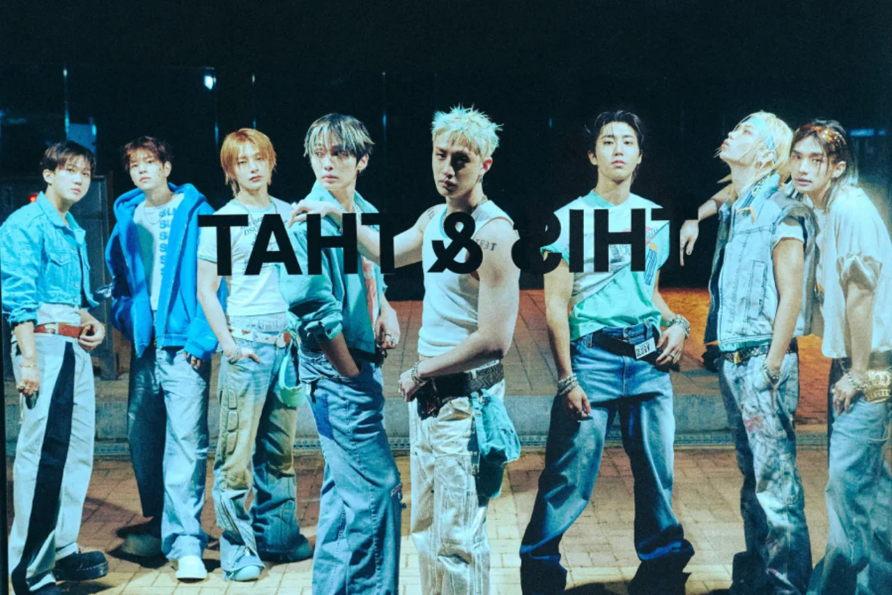 Membros do Stray Kids suando, vestindo roupas esportivas, segurando microfones sobre um palco iluminado