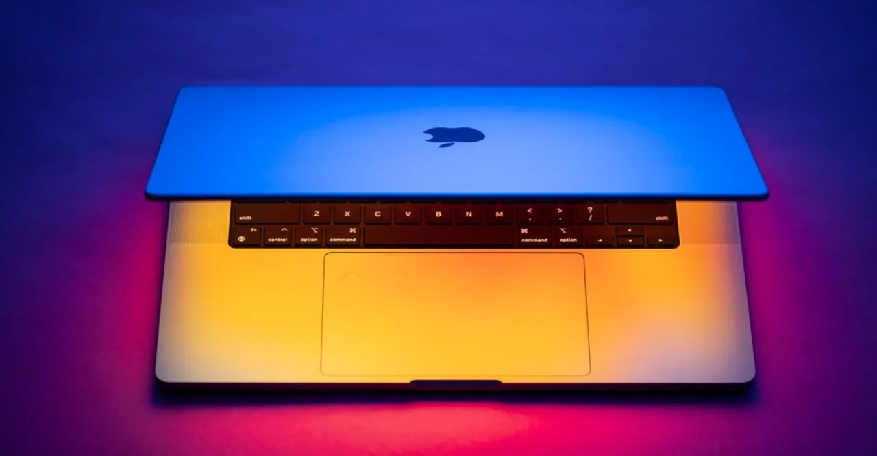 MacBook prateado da Apple com tela sensível ao toque, dedo pressionando o display e logo da Apple ao fundo