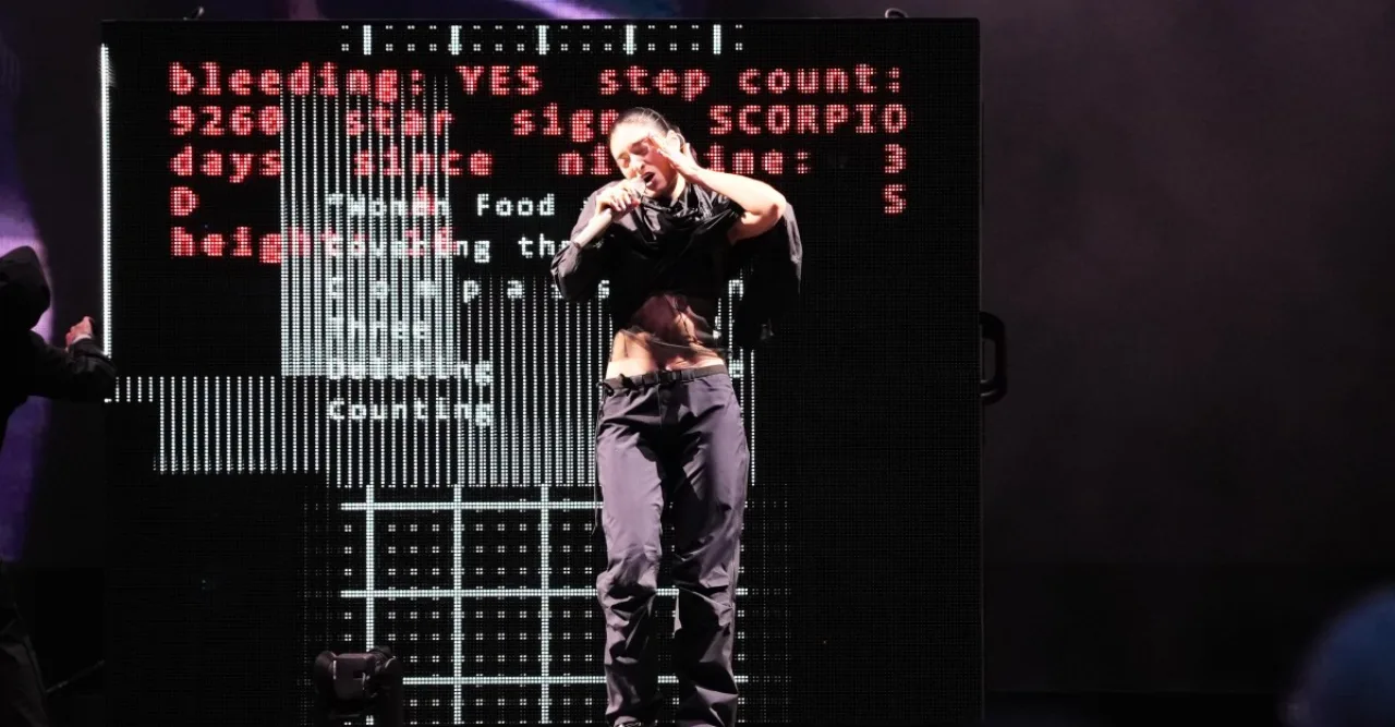 Lorde no palco, vestida de preto, segura os óculos Ray‑Ban/Meta e faz gesto de reprovação ao público