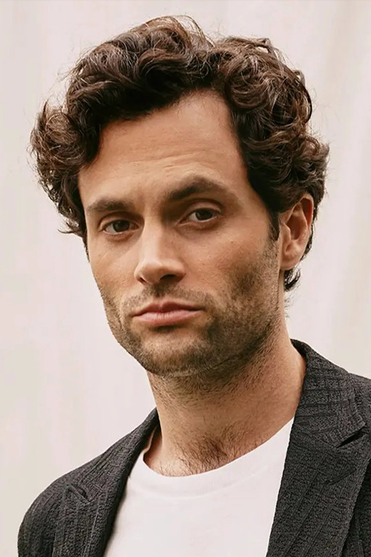 Homem de terno casual faz agachamento com halteres ao lado da TV exibindo a série de Penn Badgley