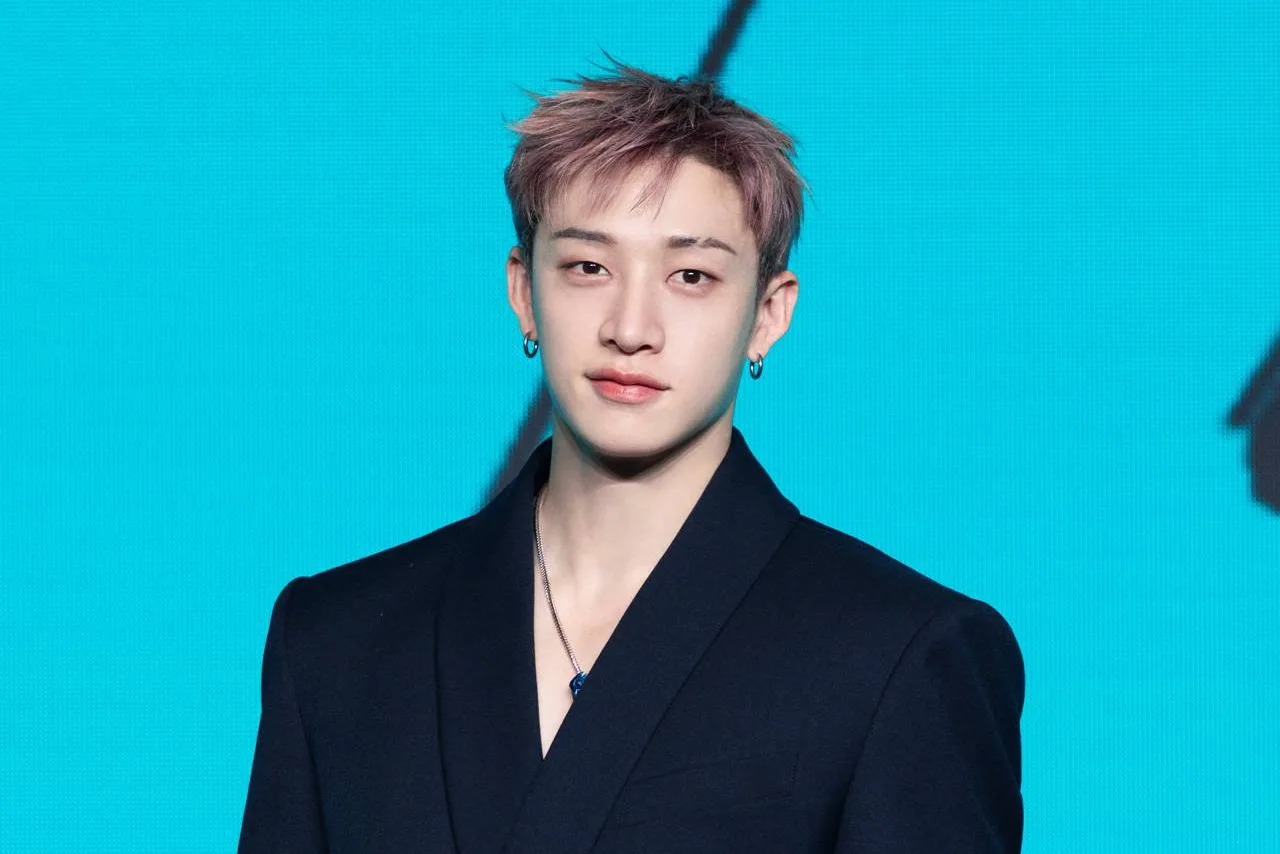 Bang Chan sorrindo ao lado de um certificado de doação, com o logo da UNICEF e do Seoul Rehabilitation Hospital ao fundo