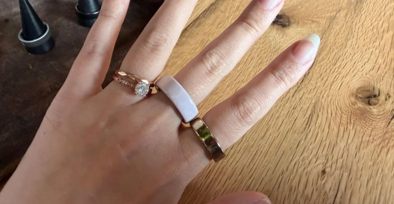 Close em mão elegante usando o novo Oura Ring 5, destacando seu design fino e discreto sobre uma mesa de madeira