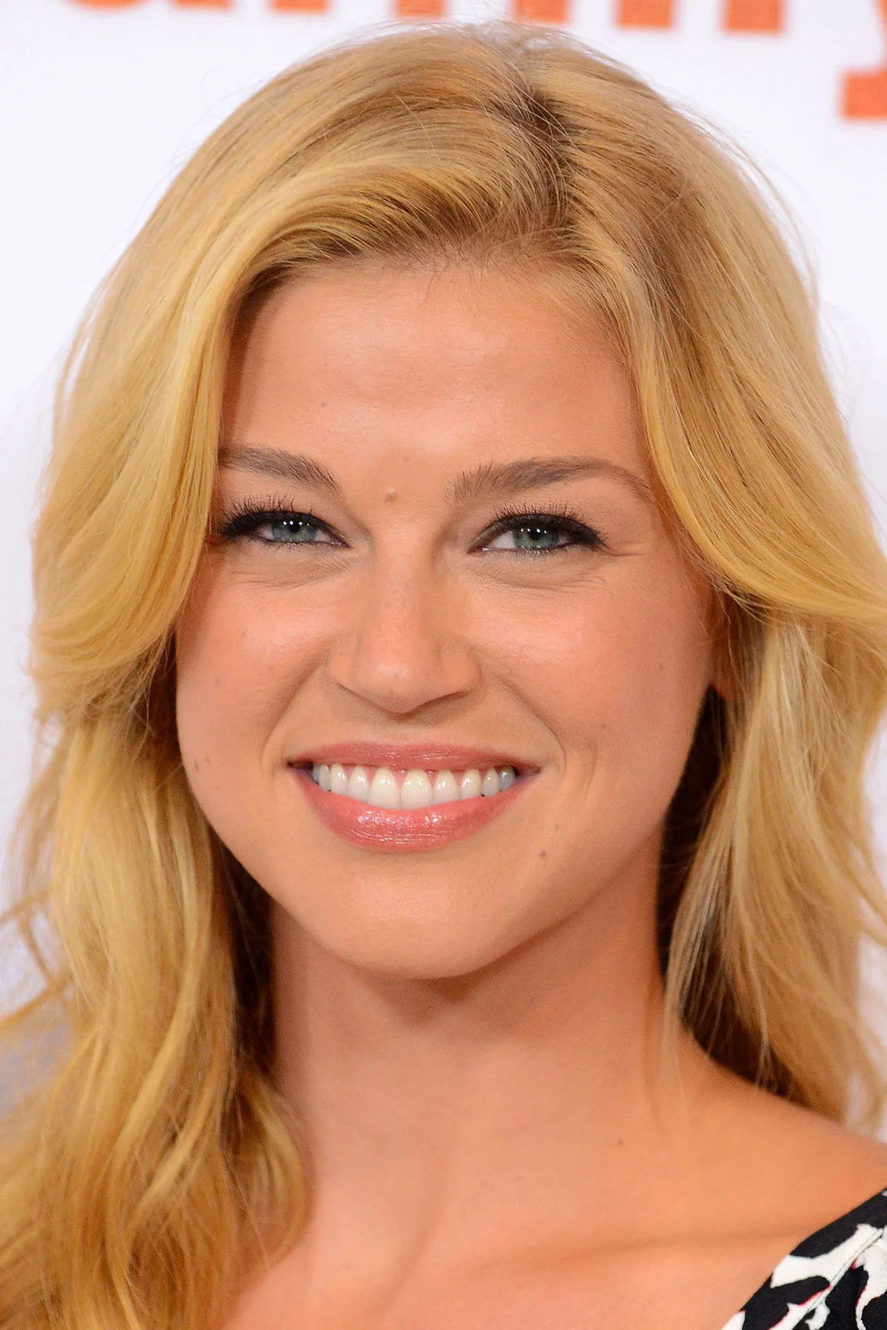 Adrianne Palicki em roupa de academia, segurando halteres ao lado de uma capa da Rogue