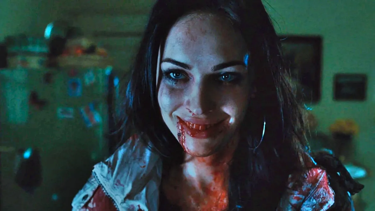Megan Fox vestindo roupa de treino preta, segurando halteres dourados ao lado de um kettlebell vermelho