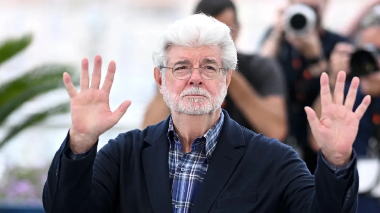 George Lucas sentado em cadeira de escritório, rodeado por halteres, colchonete de yoga e plantas verdes