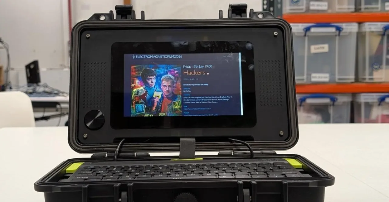 Jovem sentado no chão, laptop mini‑PC Raspberry Pi aberto, ao lado de garrafa d'água, halteres e tapete de yoga