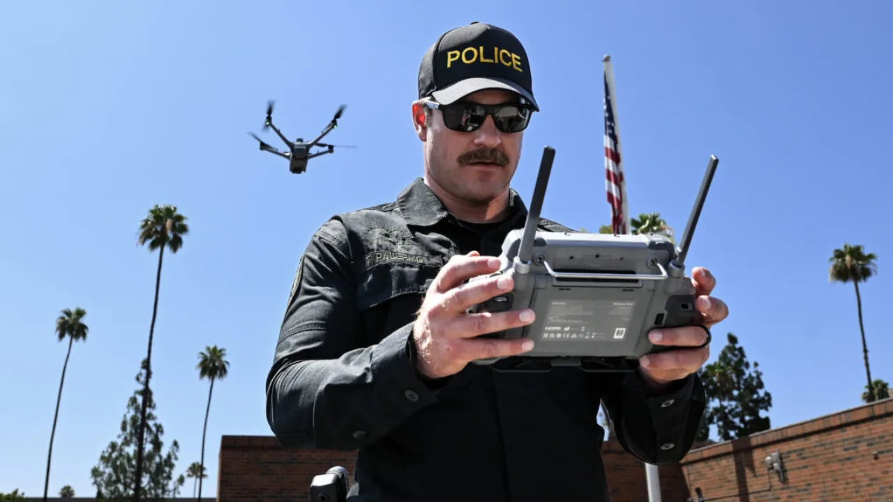 Jovem em roupa de ginástica usando smartwatch enquanto observa drone sobre parque ao pôr‑sol