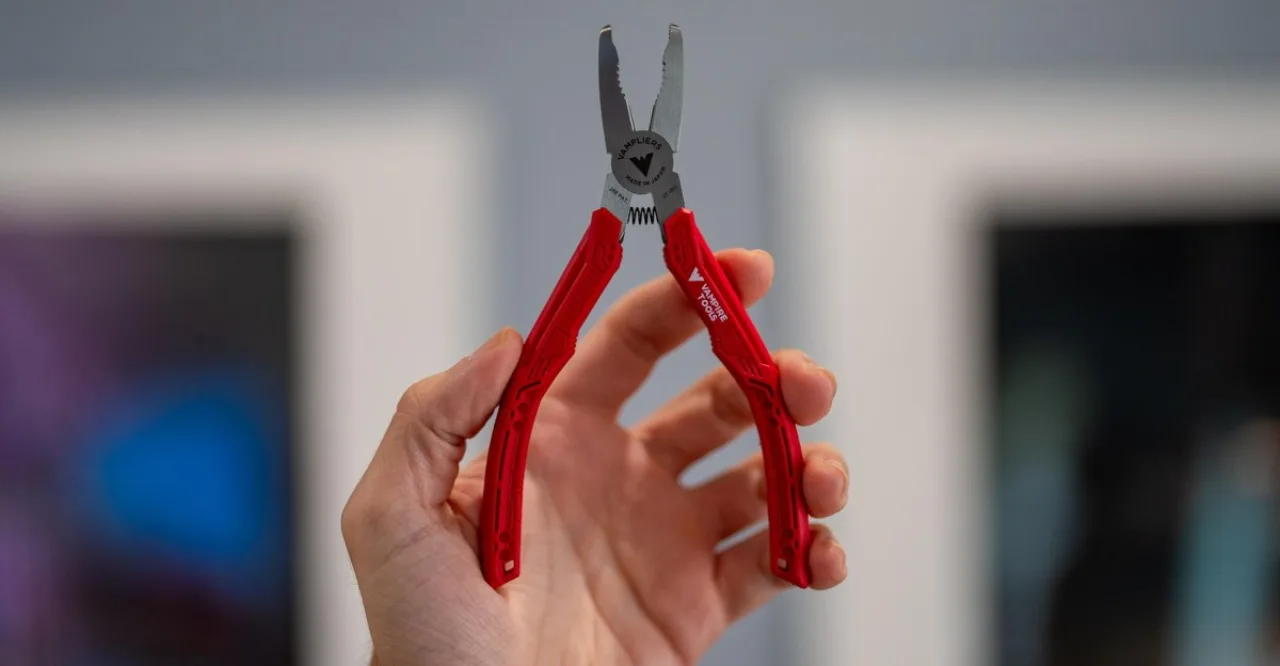 Close-up de uma mão usando vampliers para ajustar uma barra de ferro de uma estrutura metálica de equipamento de academia, com halteres e tapete de yoga ao fundo