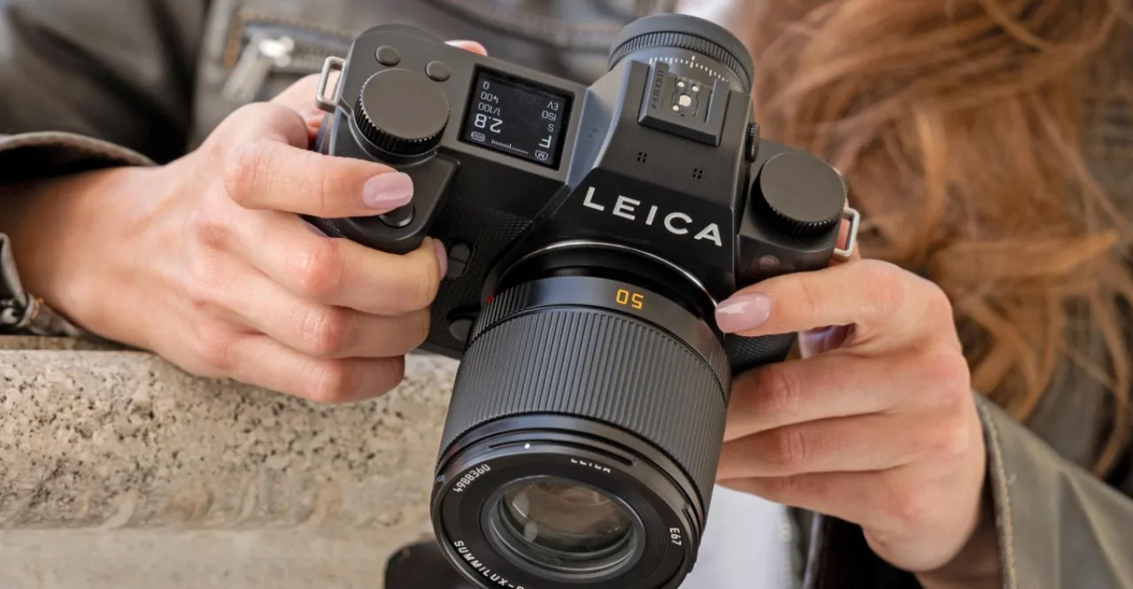 Corredor usando fone, garrafa d'água e smartwatch, ao fundo uma câmera Leica SL3‑P sobre a mesa