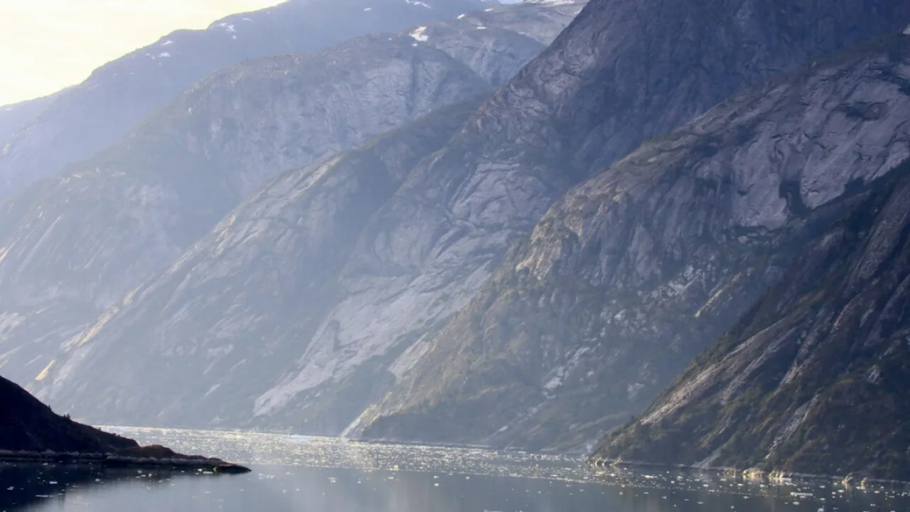 Smartwatch, barras de cereal e kit médico sobre rochas com o megatsunami de 500 metros ao fundo, no Alasca