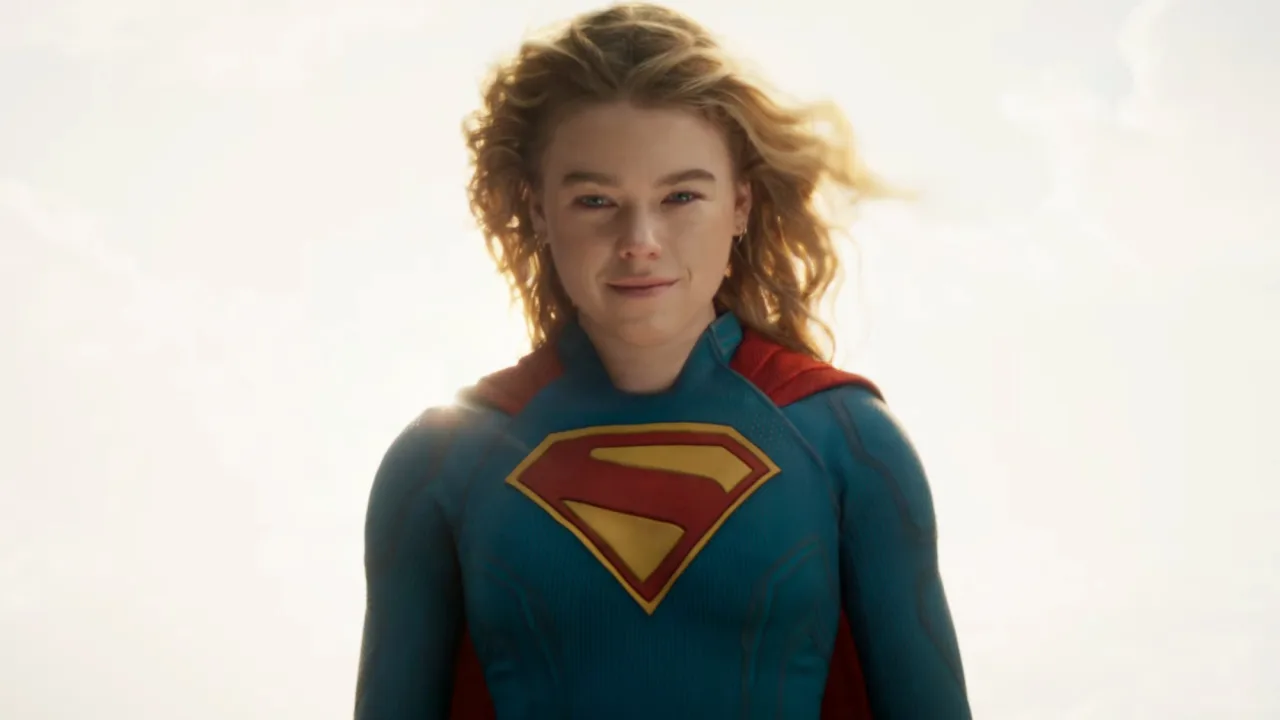 Milly Alcock vestindo a capa de Supergirl, fazendo flexão de braço em academia, com halteres ao fundo