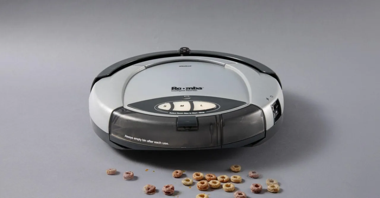 Mulher em roupa de academia limpa o chão com um Roomba enquanto faz alongamento
