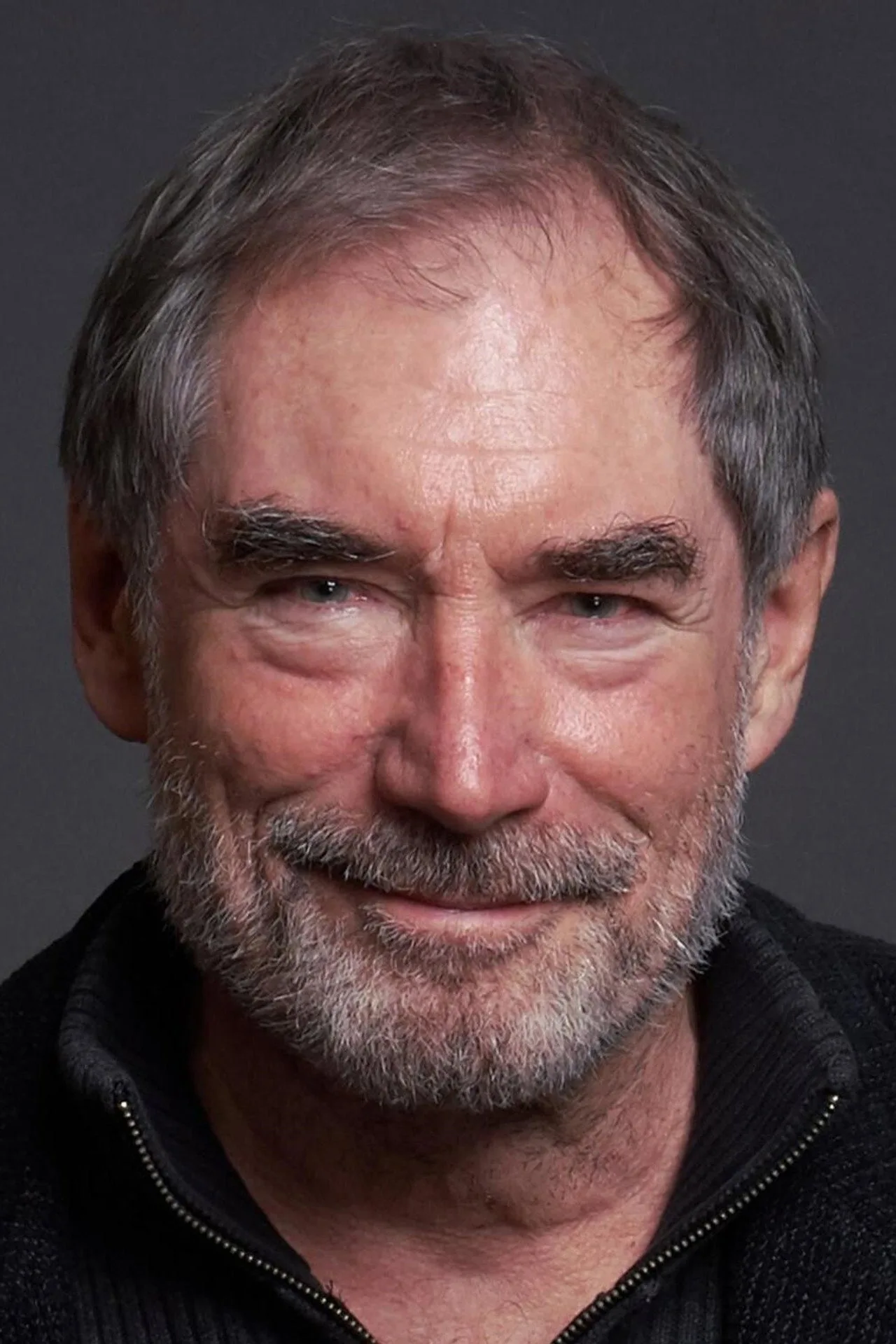 Timothy Dalton empunhando uma pistola silenciada ao lado de um carro esportivo preto, com sombras dramáticas ao fundo