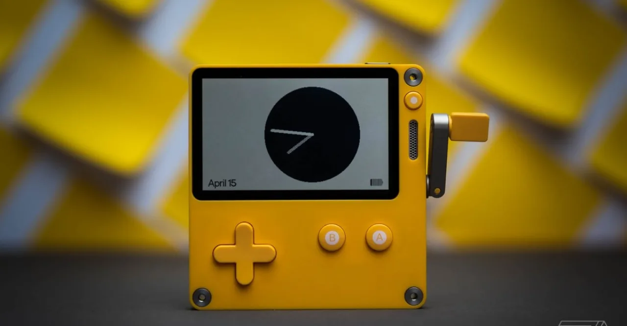 Handheld amarelo Playdate da Panic, com tela monocromática e manivela lateral, exibindo capa da nova temporada de jogos