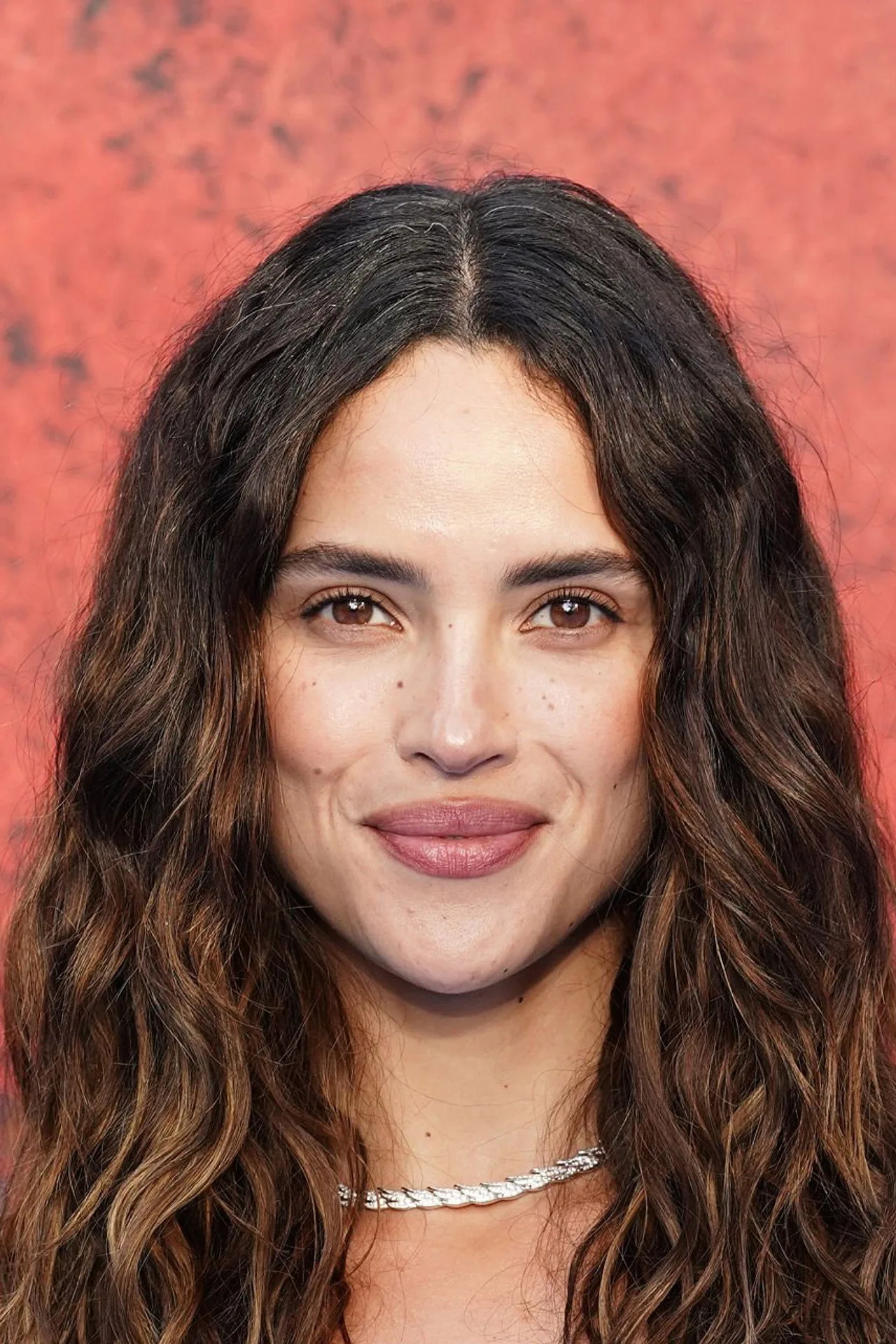 Adria Arjona levanta halteres dourados em academia, vestindo top preto e leggings, ao lado de um tapete de yoga