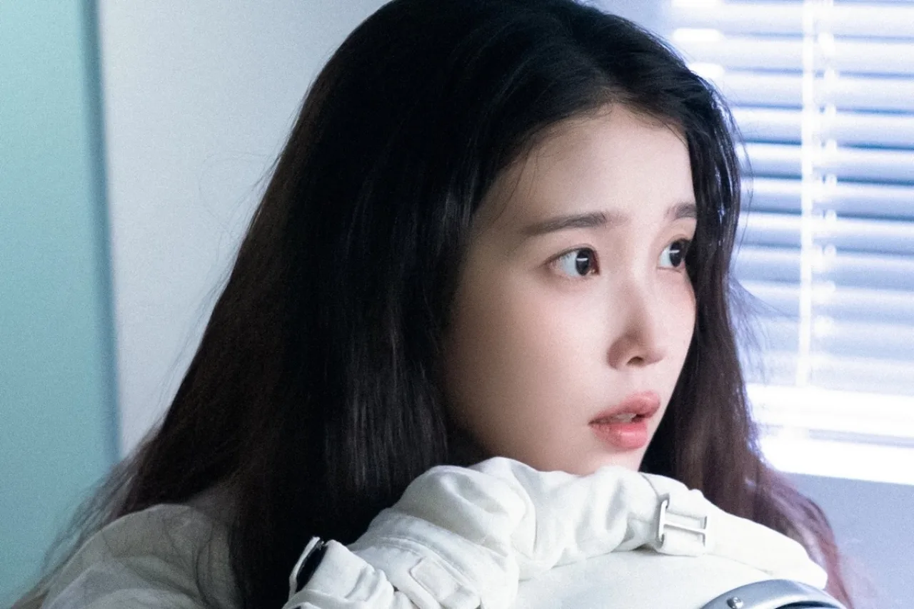 IU aparece sorrindo, vestida de branco, ao lado de um banner que exibe “200 milhões de won” e logos das ONGs