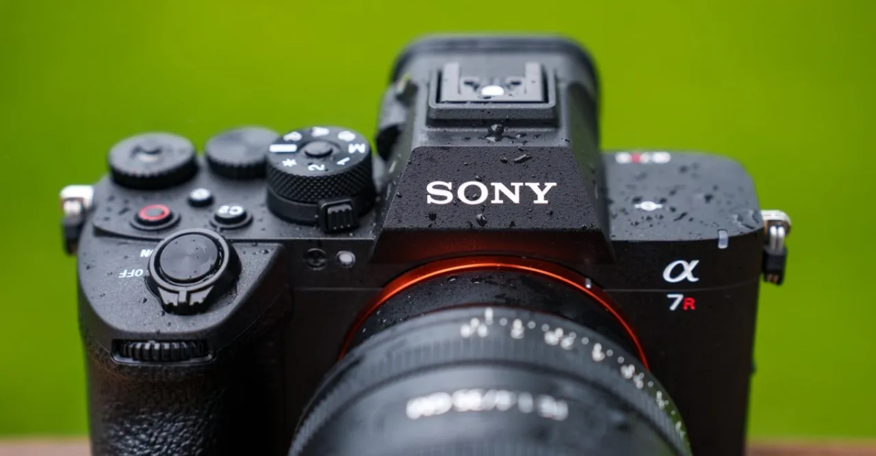 Corredor usando smartwatch, segurando a Sony A7R VI enquanto passa por trilha arborizada com garrafa de água
