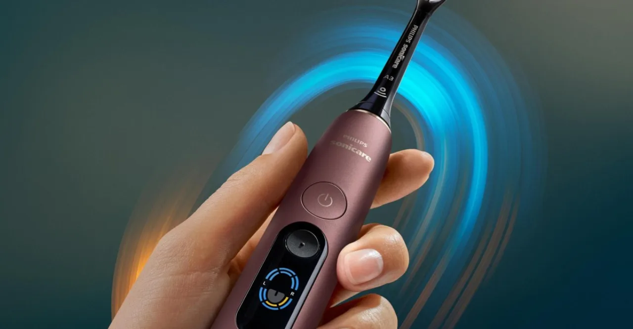 Escova elétrica Philips Sonicare DiamondClean 9900 Prestige com anel luminoso azul ao lado de um smartphone exibindo mapa de escovação