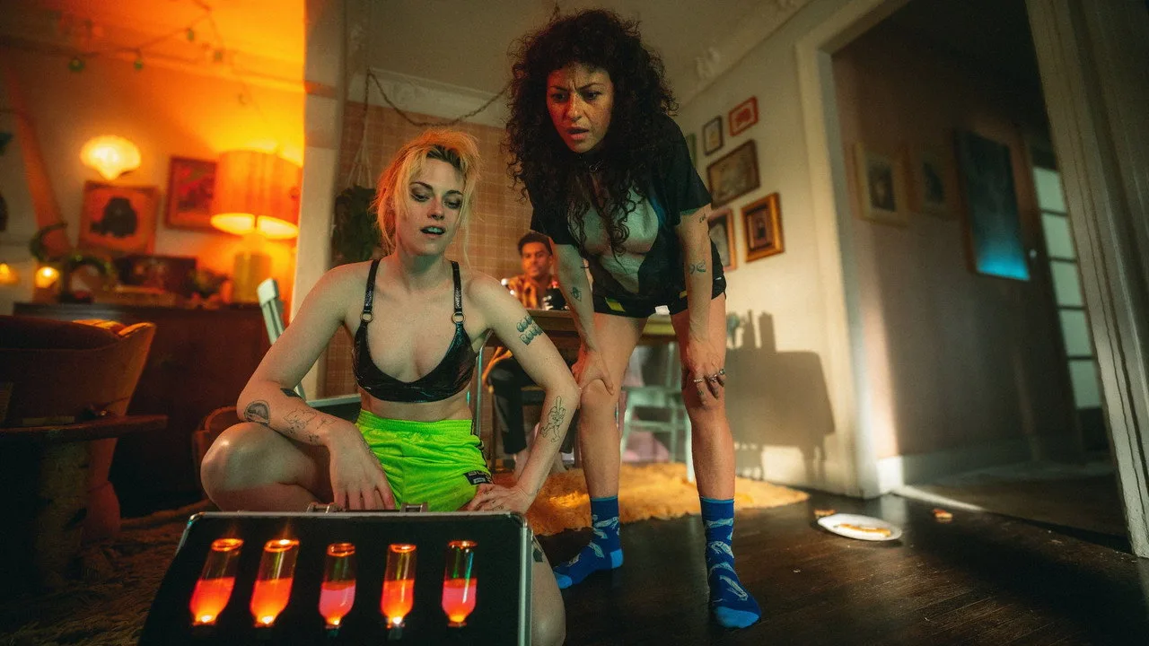 Jovem faz agachamento com halteres, enquanto assiste The Wrong Girls no tablet, ao lado de água e banana