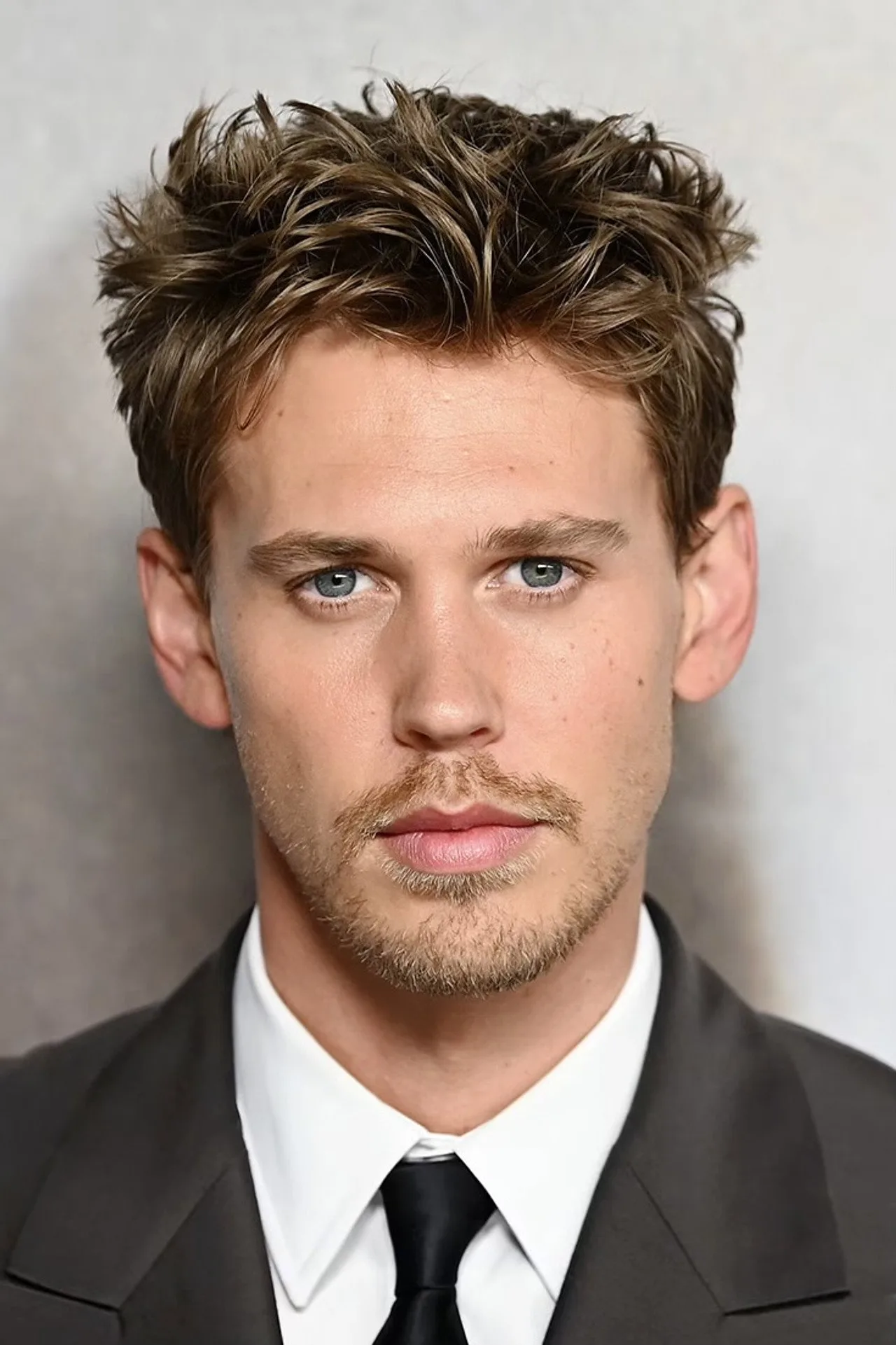 Austin Butler em roupa de treino, segurando a espada de Wil Ohmsford, cercado por halteres e um quadro motivacional