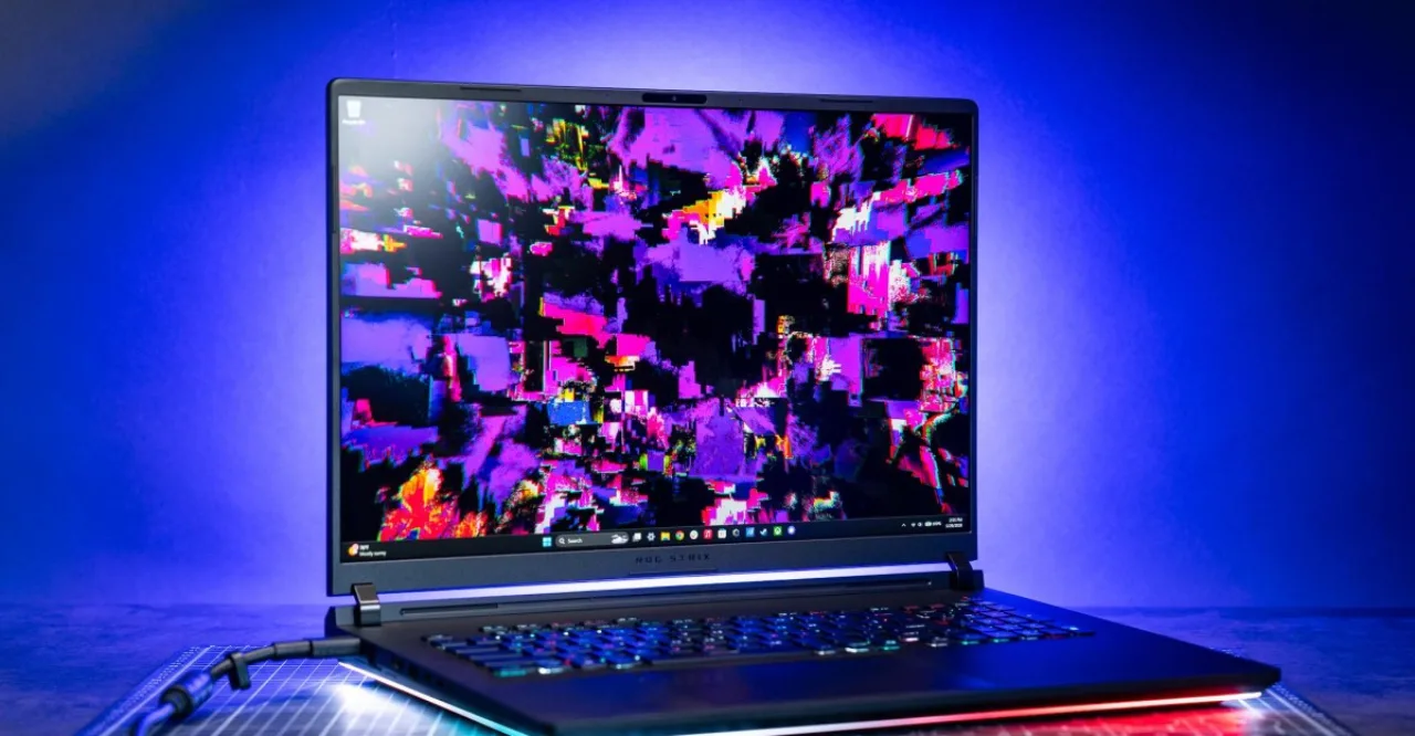 Close-up de um laptop gamer com tela OLED exibindo gráficos vibrantes ao lado de um mouse ergonômico e teclado RGB