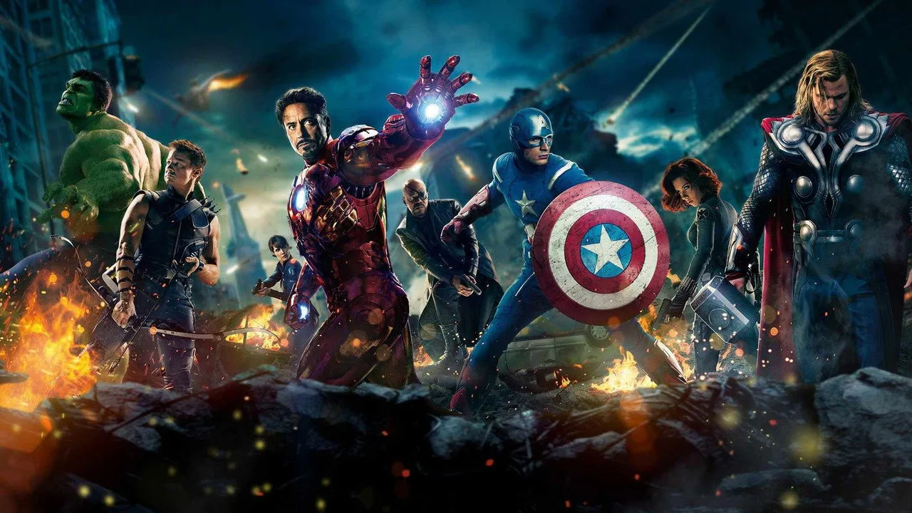 Homem em traje azul levantando barra ao lado de quadrinhos antigos da Guerra Kree‑Skrull na parede