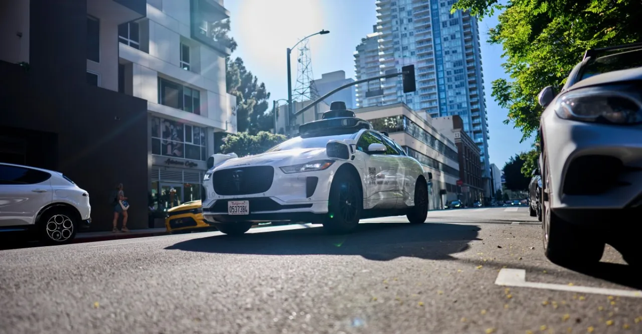 Waymo robotaxi branco com logo azul ao lado de viatura policial, enquanto adolescentes mostram uma arma de brinquedo