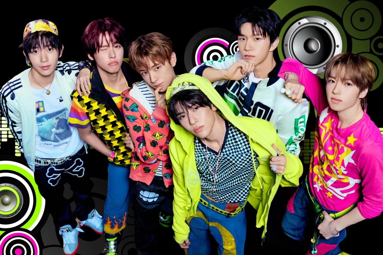 Membros de NCT WISH posam sorrindo segurando o mini‑álbum I SPY, com o logotipo da banda ao fundo