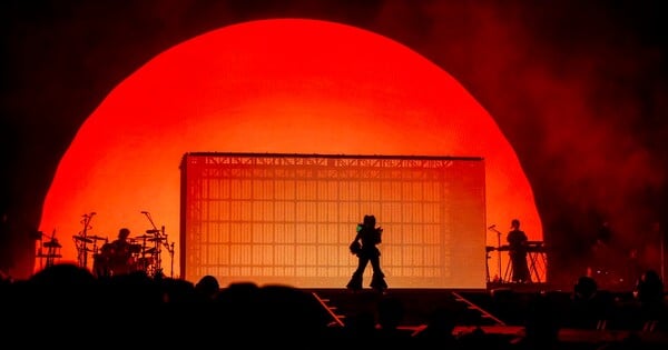 Jovem japonesa em roupa esportiva vibra ao som de 'Enter Sandman' em um palco iluminado, segurando fones e garrafa d'água