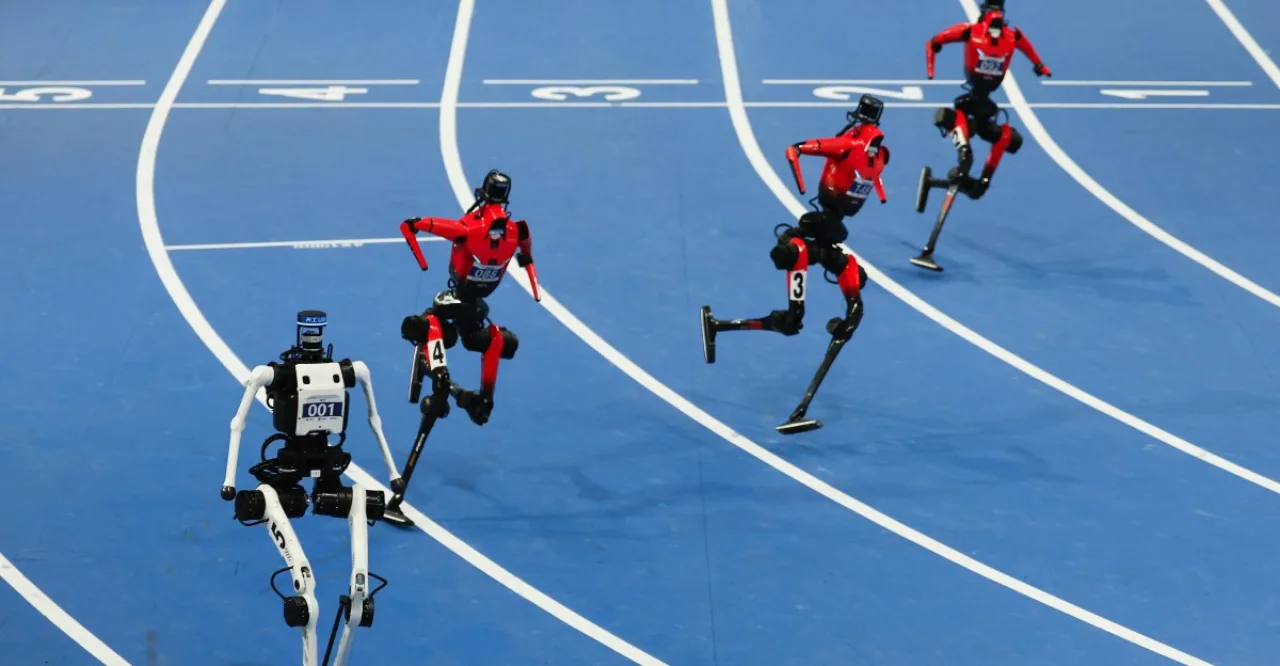 Robôs chineses em largada, com blocos de partida, pista de atletismo e cronômetro digital ao fundo