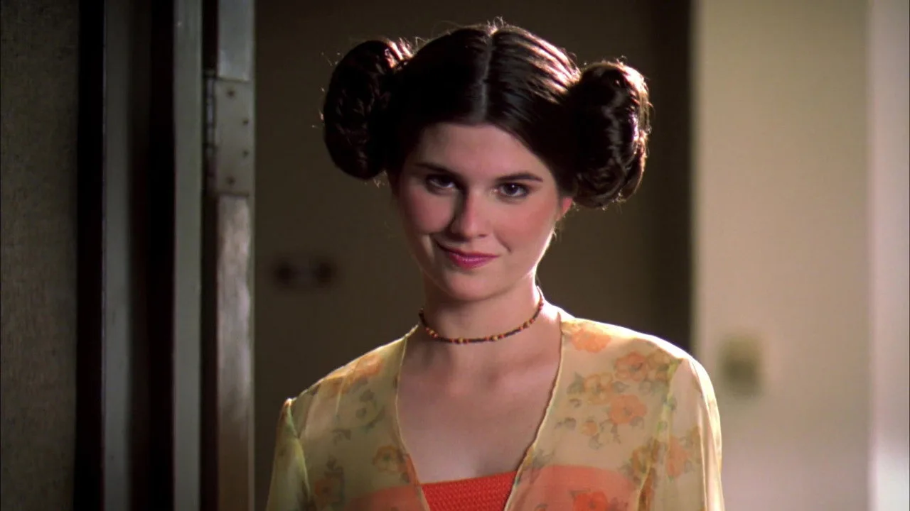 Um cineasta indie segurando uma câmera vintage ao lado de um haltere, com um pôster de Star Wars ao fundo