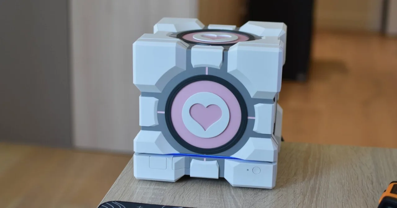 Steam Machine coberta pelo case Companion Cube da Dbrand, ao lado de um controle e um copo de água sobre a mesa