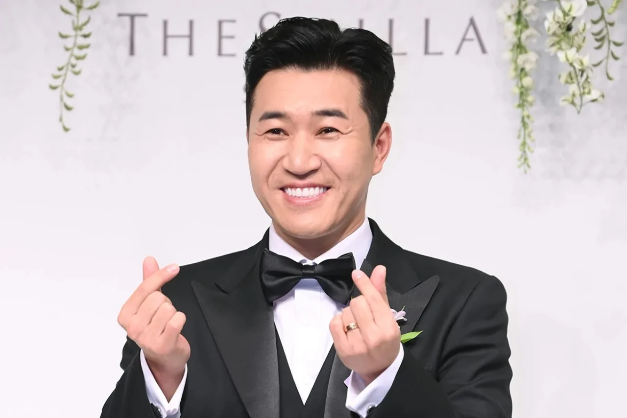 Kim Jong Min abraça a esposa, que exibe a barriga de 17 semanas, diante do letreiro do programa Return Superman