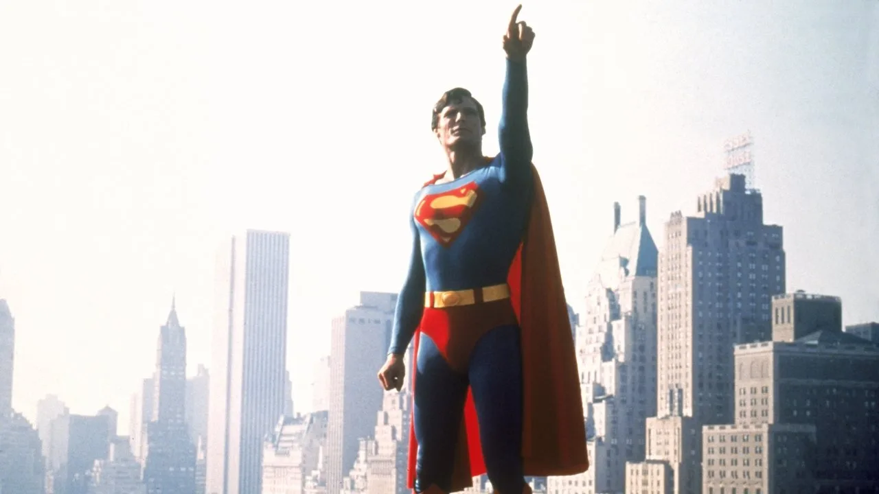 Christopher Reeve, ainda de capa de Superman, deitado sobre um banco de set, exibindo músculos definidos e expressão de cansaço